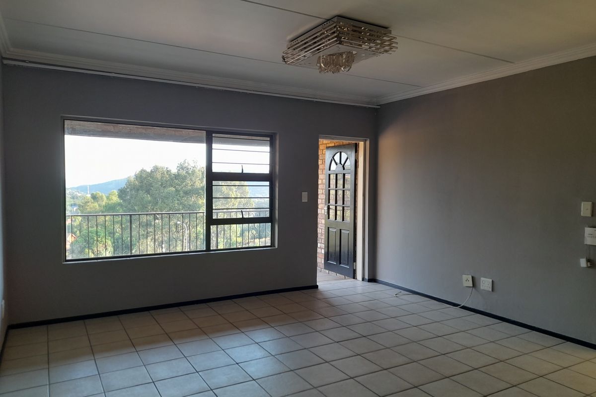An empty, neutrally painted living room featuring tiled flooring, a large window with security bars, and direct access to an outdoor balcony area.