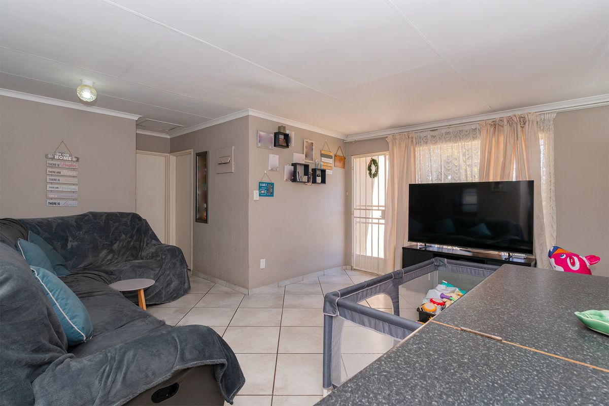 A functional living room featuring tiled flooring, coved ceilings, and direct access to an exterior security gate.