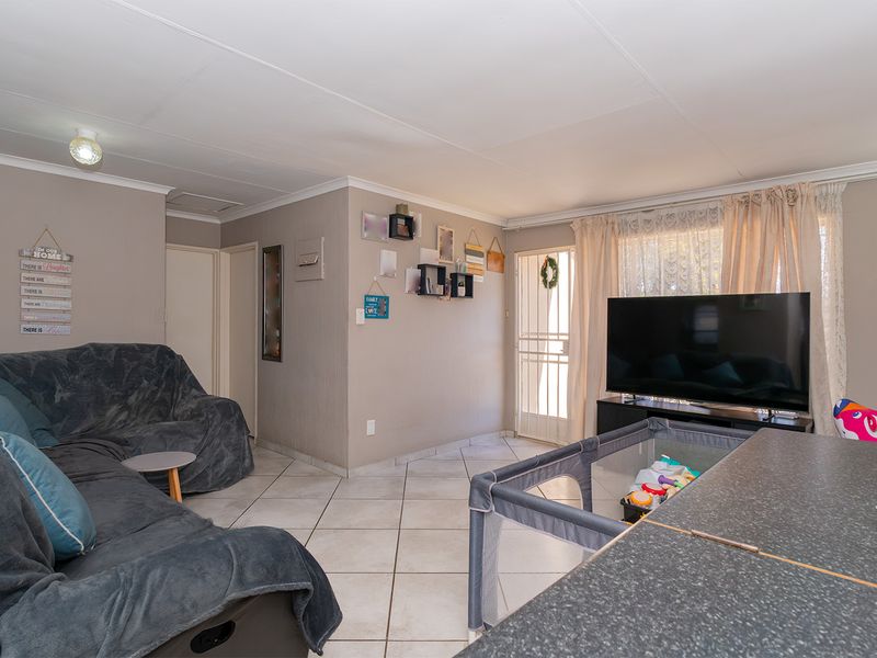 A functional living room featuring tiled flooring, coved ceilings, and direct access to an exterior security gate.