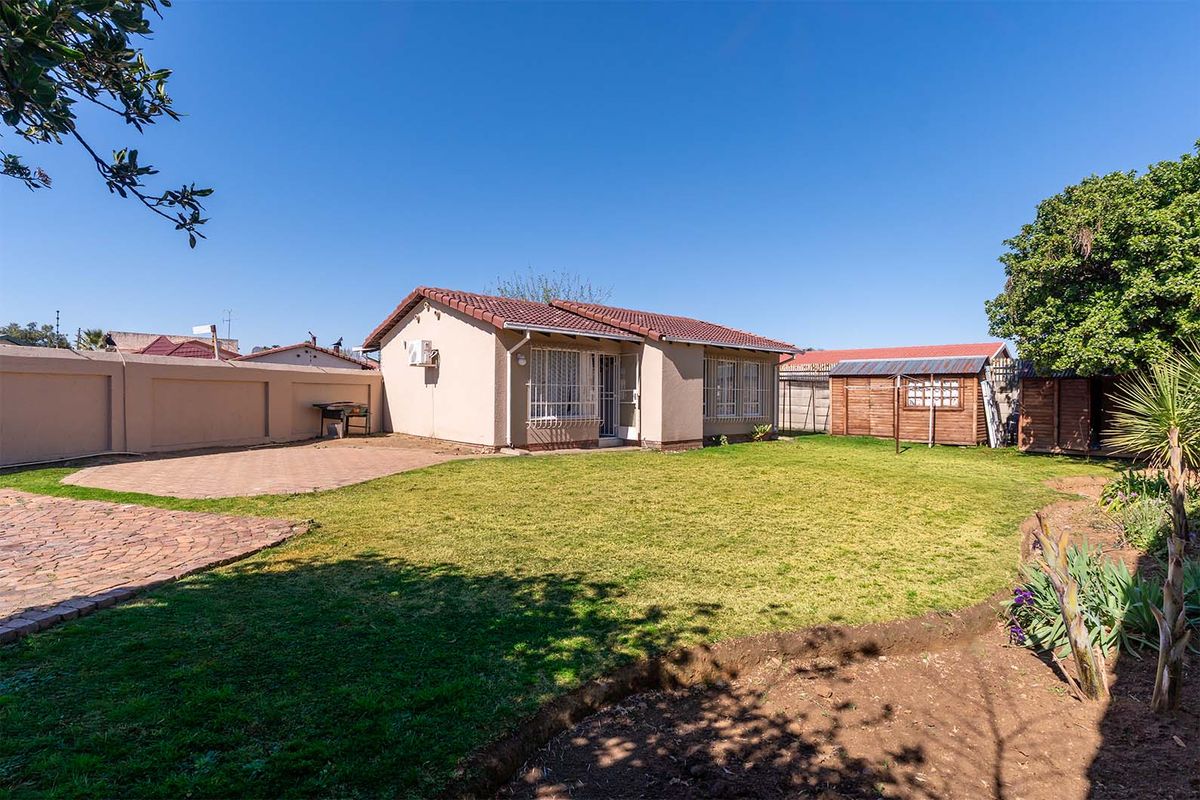 Rear view of the house featuring a paved patio area, a well-maintained lawn, perimeter walling, and a detached garden shed.