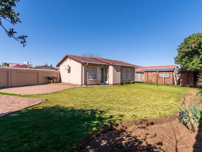 Rear view of the house featuring a paved patio area, a well-maintained lawn, perimeter walling, and a detached garden shed.