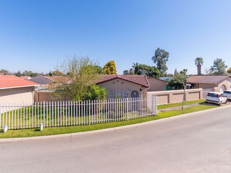 A street-level view of a residential property featuring a tiled roof, perimeter fencing, and a paved driveway area.