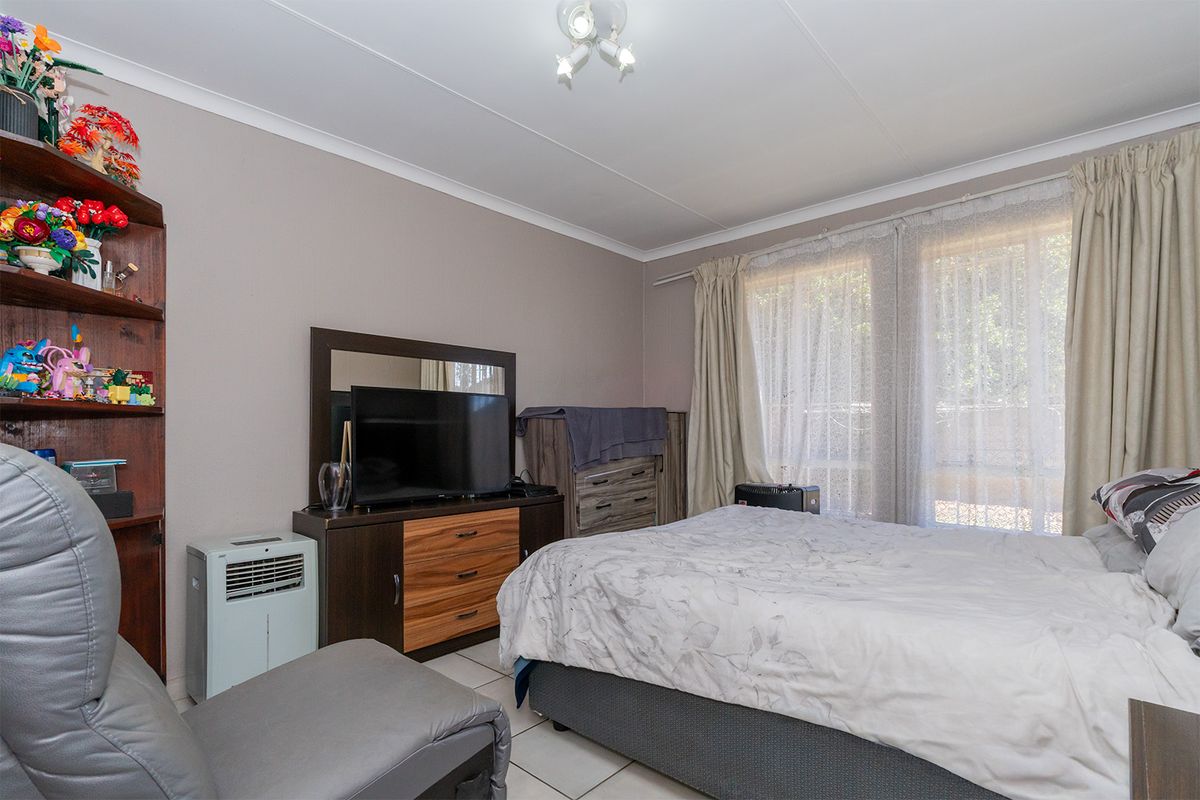 A functional bedroom featuring tiled flooring, neutral wall finishes, and large windows with curtain tracks, providing natural light and a comfortable living space.