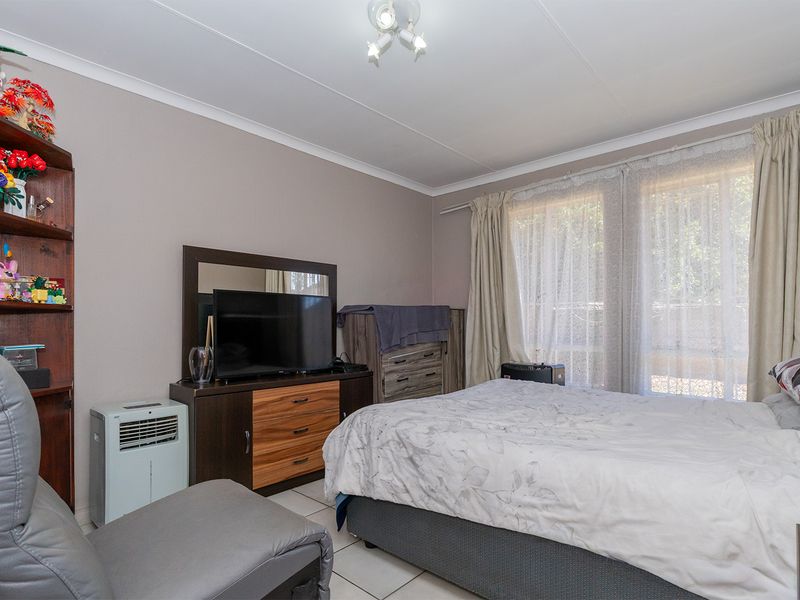 A functional bedroom featuring tiled flooring, neutral wall finishes, and large windows with curtain tracks, providing natural light and a comfortable living space.