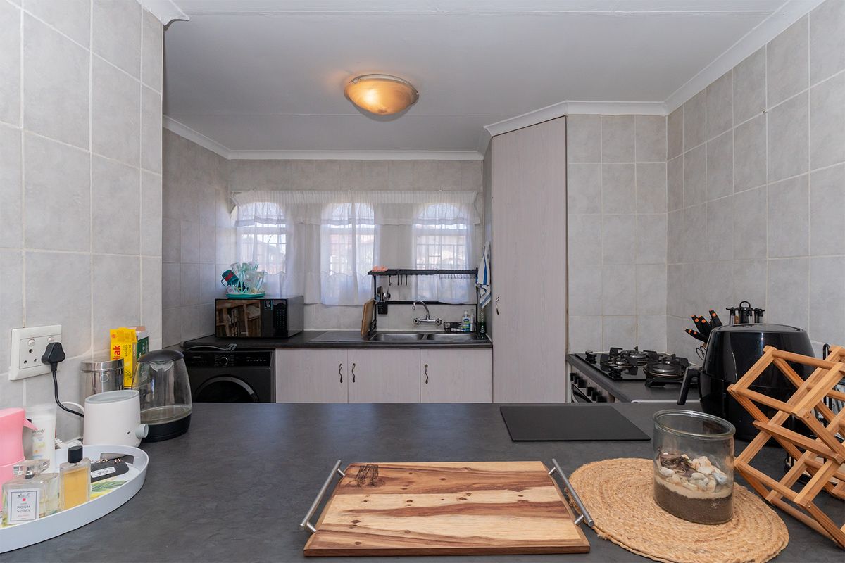 A functional kitchen featuring tiled splashbacks, built-in cabinetry, a gas hob, and integrated laundry plumbing, offering a practical layout for daily use.