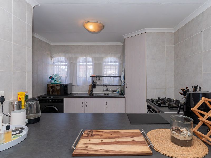 A functional kitchen featuring tiled splashbacks, built-in cabinetry, a gas hob, and integrated laundry plumbing, offering a practical layout for daily use.