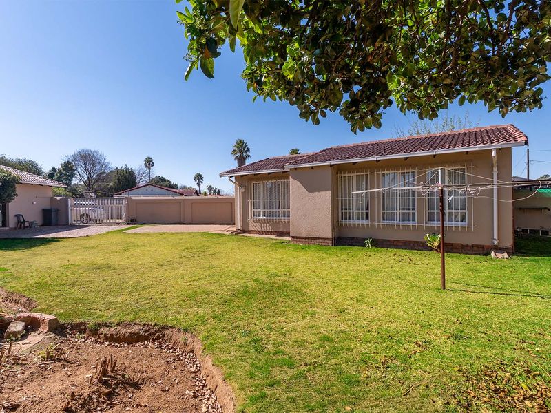 Rear view of the property featuring a spacious lawn, paved driveway, perimeter wall, and a tiled roof house with security bars on windows.
