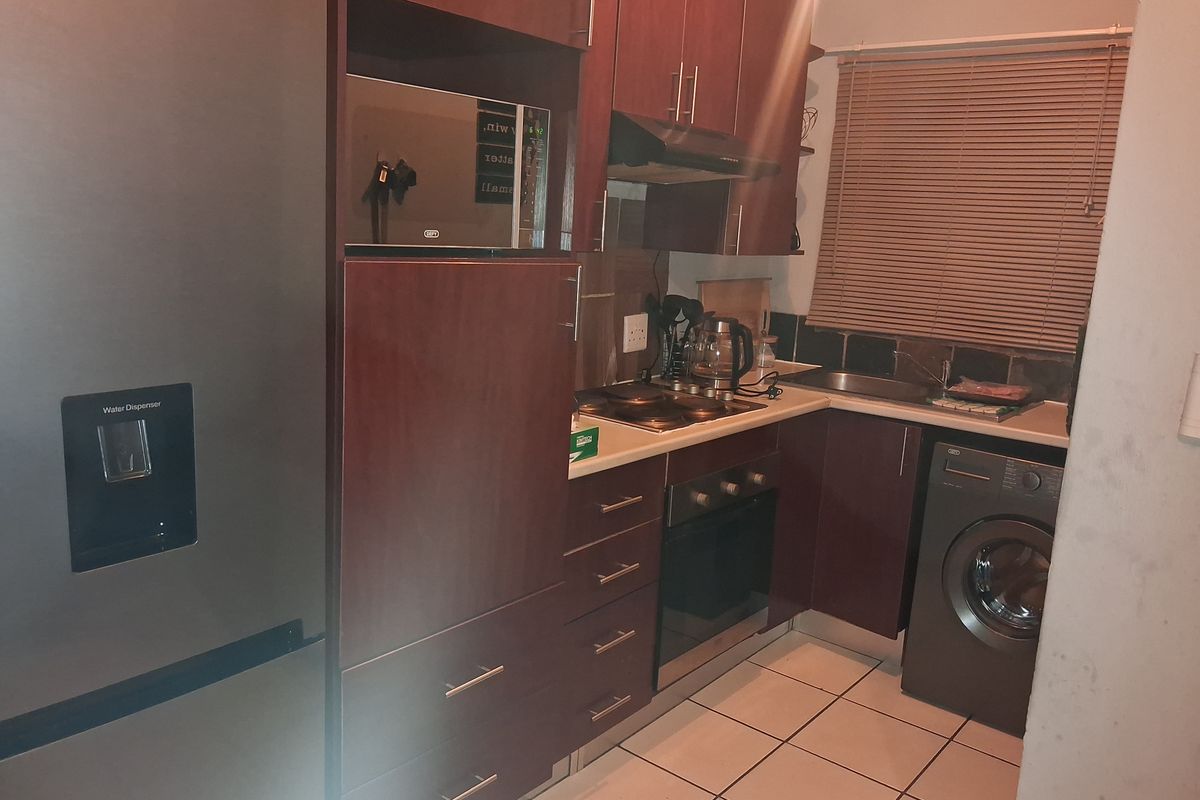 Compact kitchen featuring dark wood cabinetry, built-in oven and hob, extractor fan, integrated microwave, and tiled flooring with a functional layout.