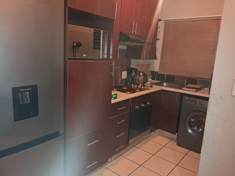 Compact kitchen featuring dark wood cabinetry, built-in oven and hob, extractor fan, integrated microwave, and tiled flooring with a functional layout.