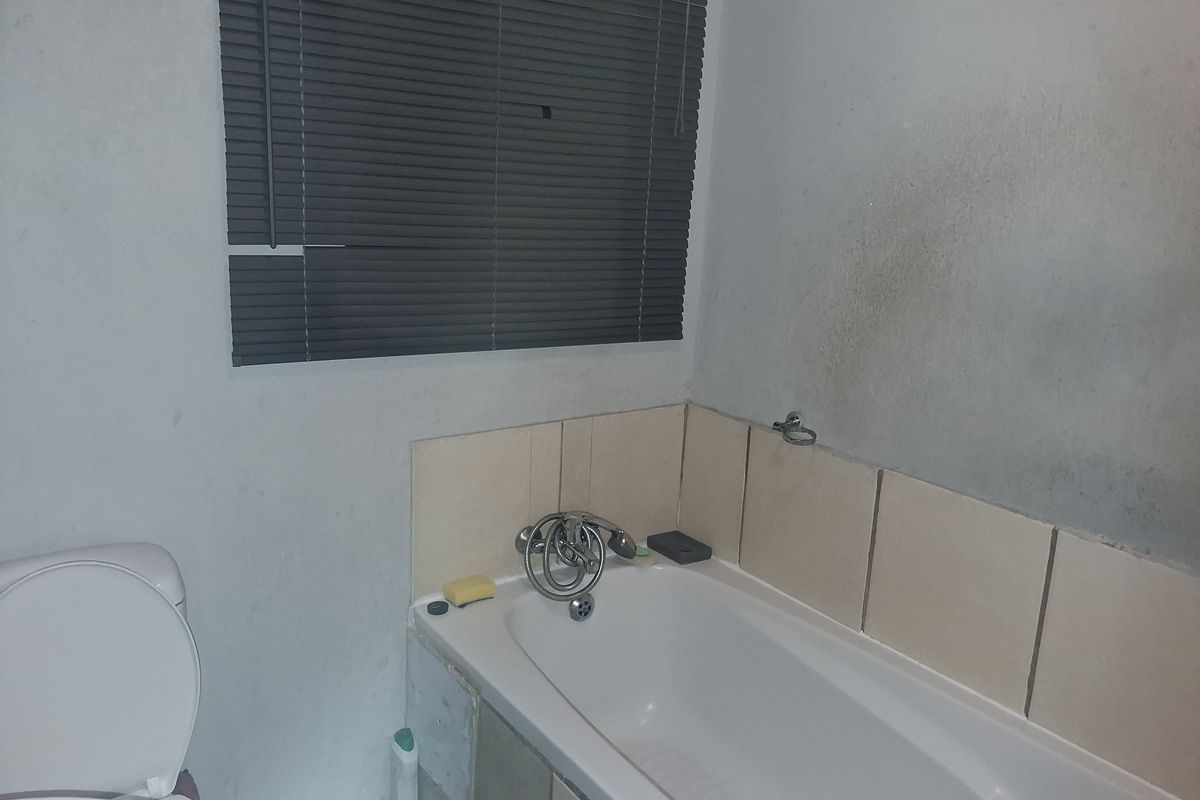 A bathroom featuring a bathtub with tiled splashback, toilet, and window blinds. The space requires cosmetic updates and wall repairs.