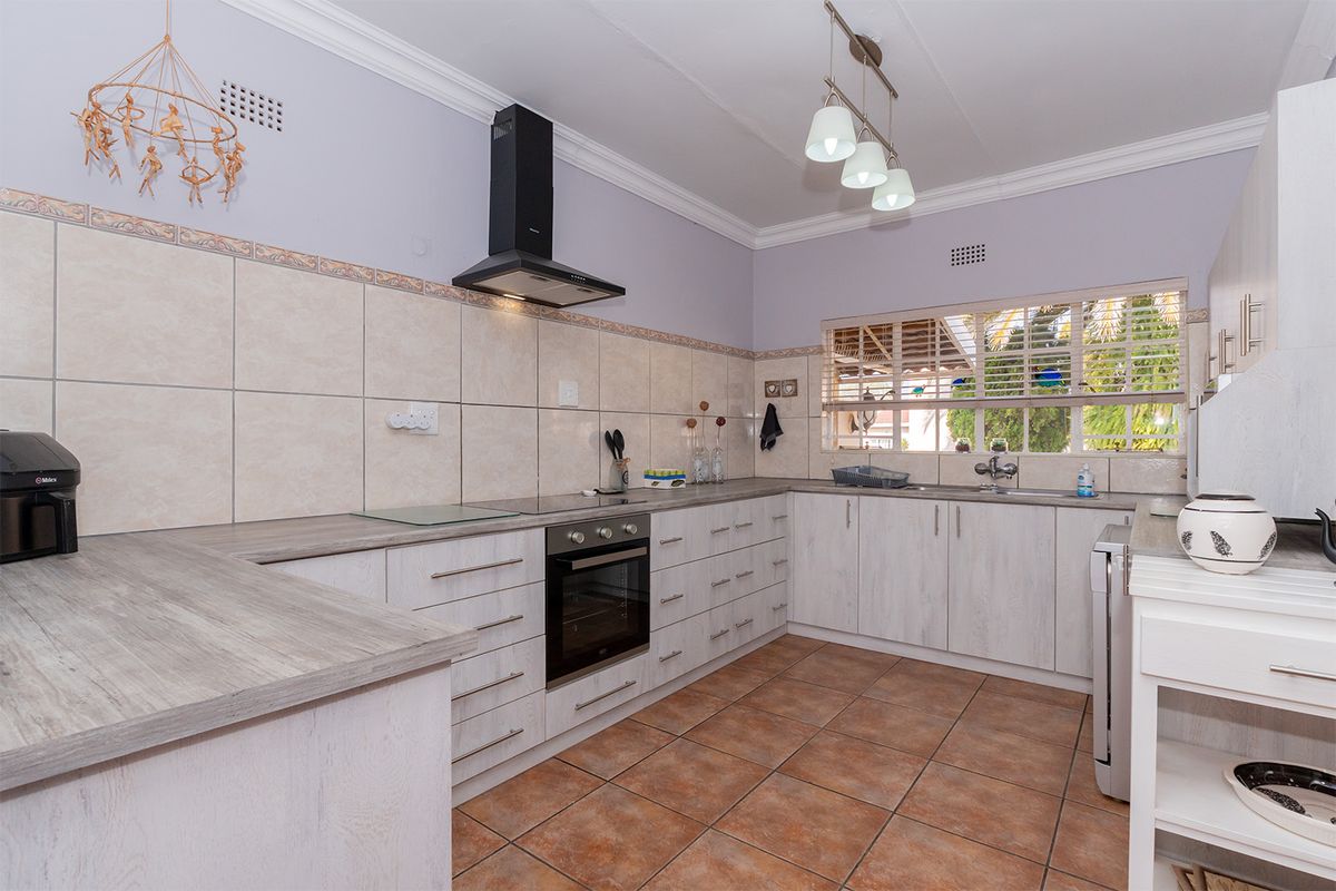 A functional kitchen featuring light wood-grain cabinetry, laminate countertops, built-in oven with extractor fan, and tiled flooring with a neutral backsplash.