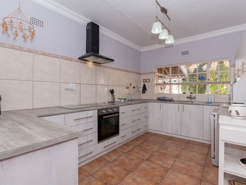 A functional kitchen featuring light wood-grain cabinetry, laminate countertops, built-in oven with extractor fan, and tiled flooring with a neutral backsplash.