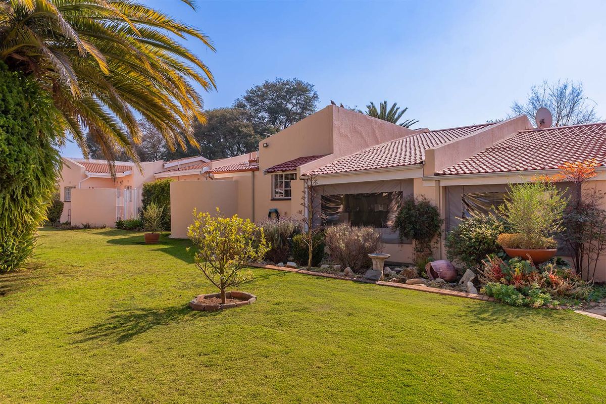 A well-maintained rear exterior view of the apartment featuring a landscaped garden, lawn, and a covered patio area with terracotta roof tiles.