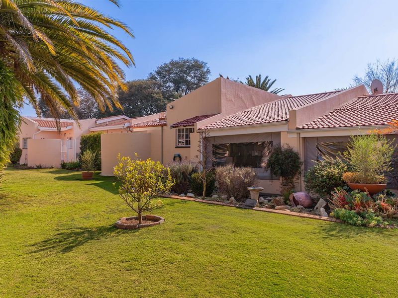 A well-maintained rear exterior view of the apartment featuring a landscaped garden, lawn, and a covered patio area with terracotta roof tiles.