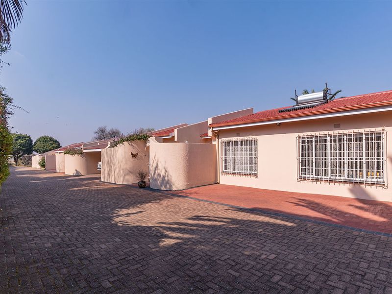 Front exterior view of a residential apartment complex featuring a paved driveway, stucco facade, and security bars on windows.