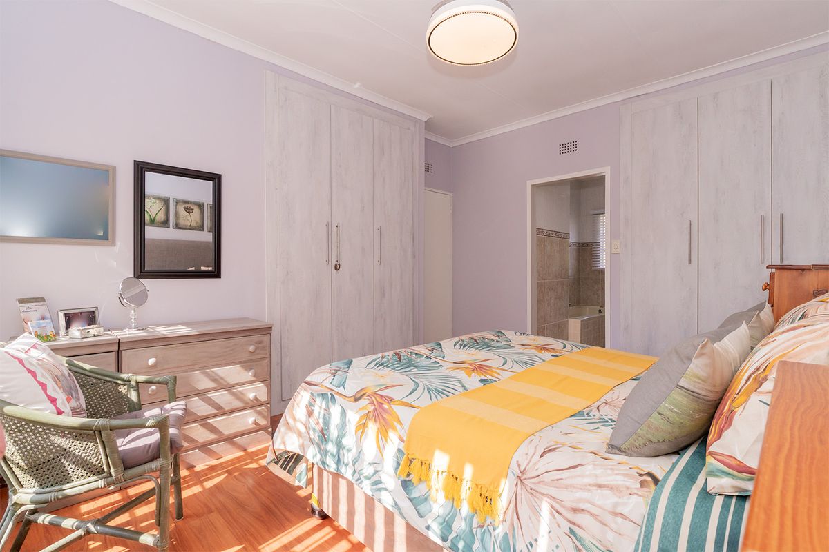 A well-maintained bedroom featuring laminate flooring, ample built-in cupboard storage, and direct access to an en-suite bathroom.