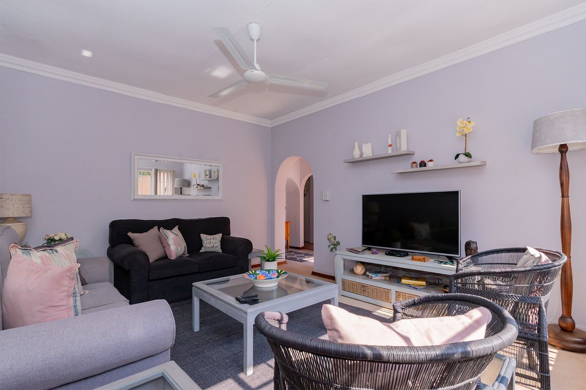 A comfortable living room featuring a ceiling fan, crown molding, and an arched doorway leading to the rest of the apartment.