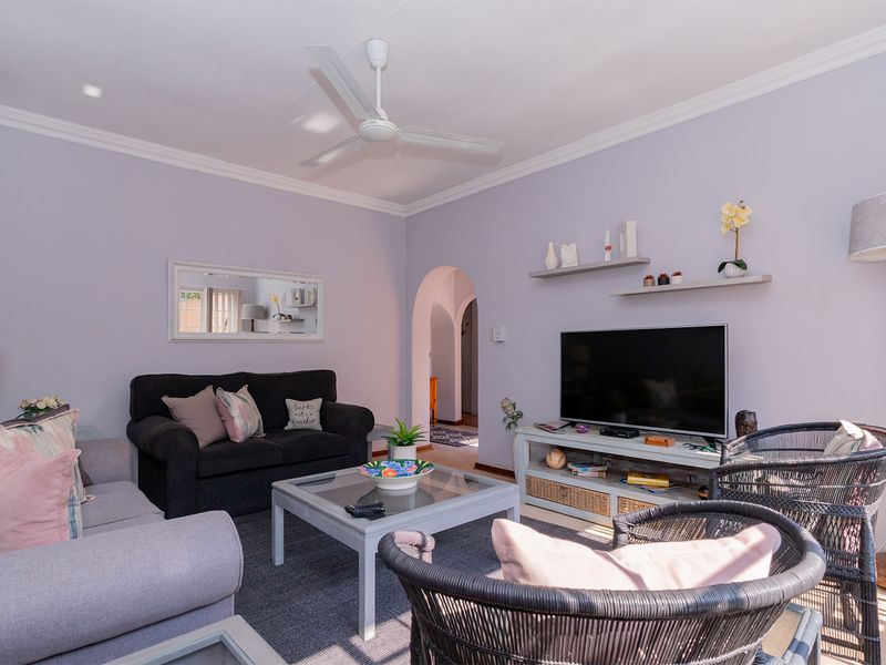 A comfortable living room featuring a ceiling fan, crown molding, and an arched doorway leading to the rest of the apartment.