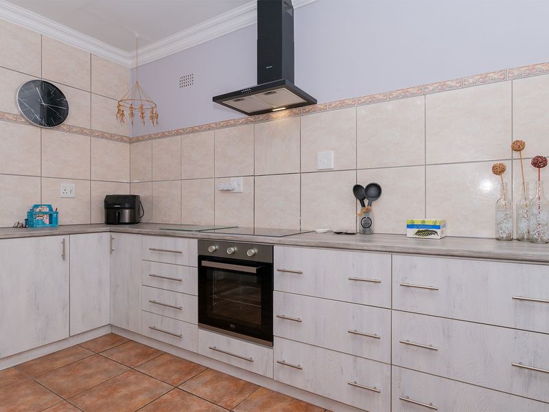 A functional kitchen featuring light wood-grain cabinetry, laminate countertops, a built-in oven with electric hob, and a modern black extractor fan.
