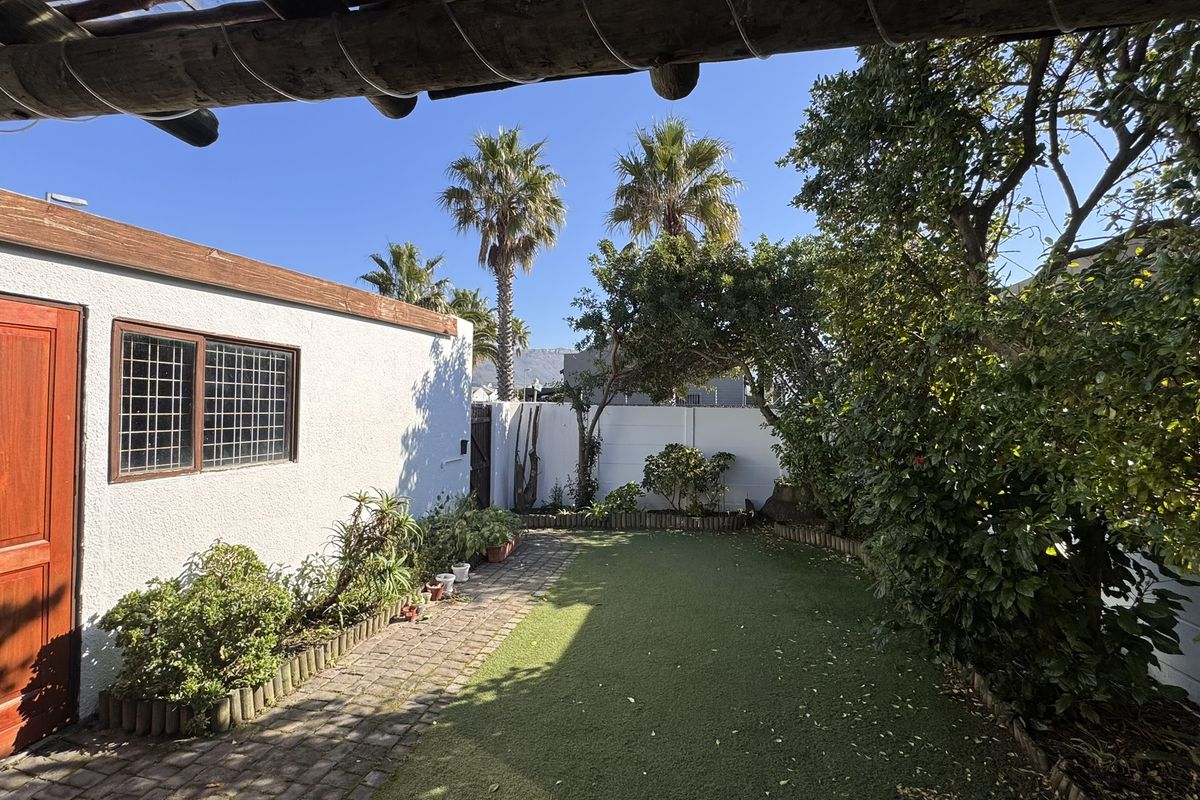 A private rear garden featuring an artificial lawn, paved walkway, and a timber pergola, enclosed by a secure boundary wall.
