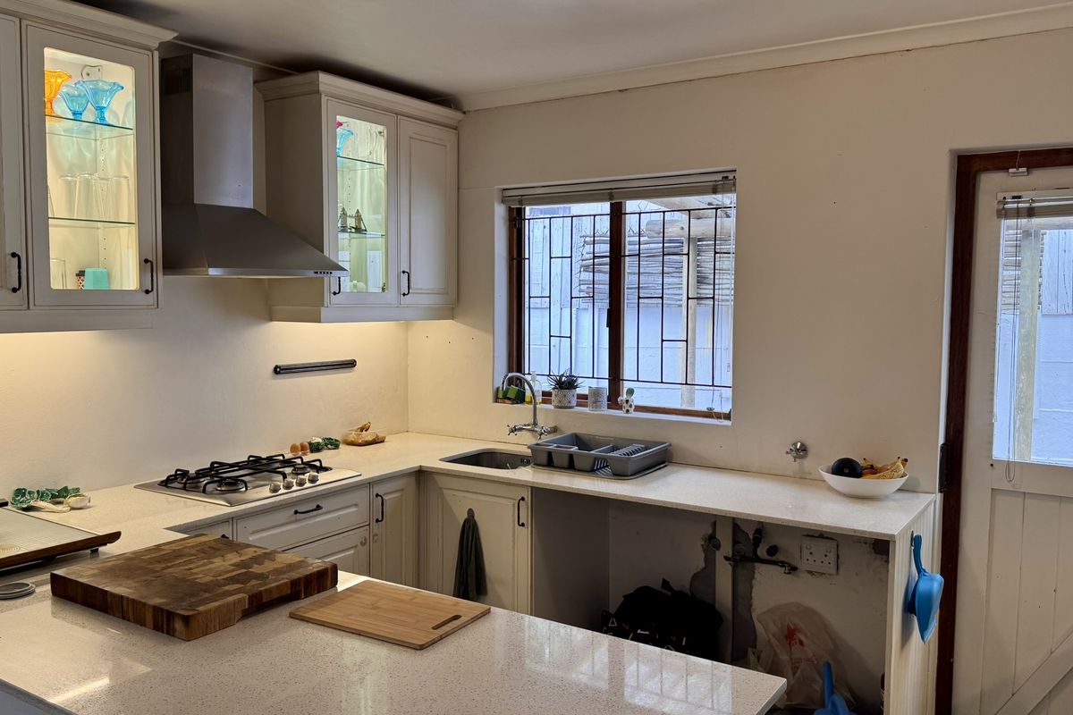 A functional kitchen featuring quartz countertops, a gas hob, stainless steel extractor, and glass-fronted cabinetry, with an open space for an under-counter appliance.
