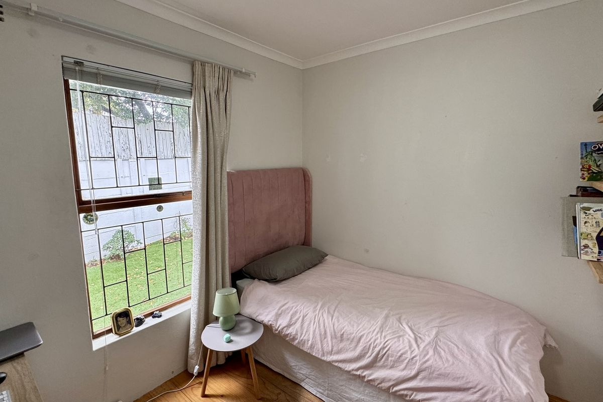 A compact bedroom featuring timber flooring, a window with security bars, and built-in wall shelving.