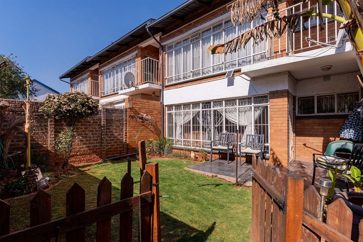 Rear view of a townhouse featuring a private garden, tiled patio area, and upper-level balcony with brick facade and security features.