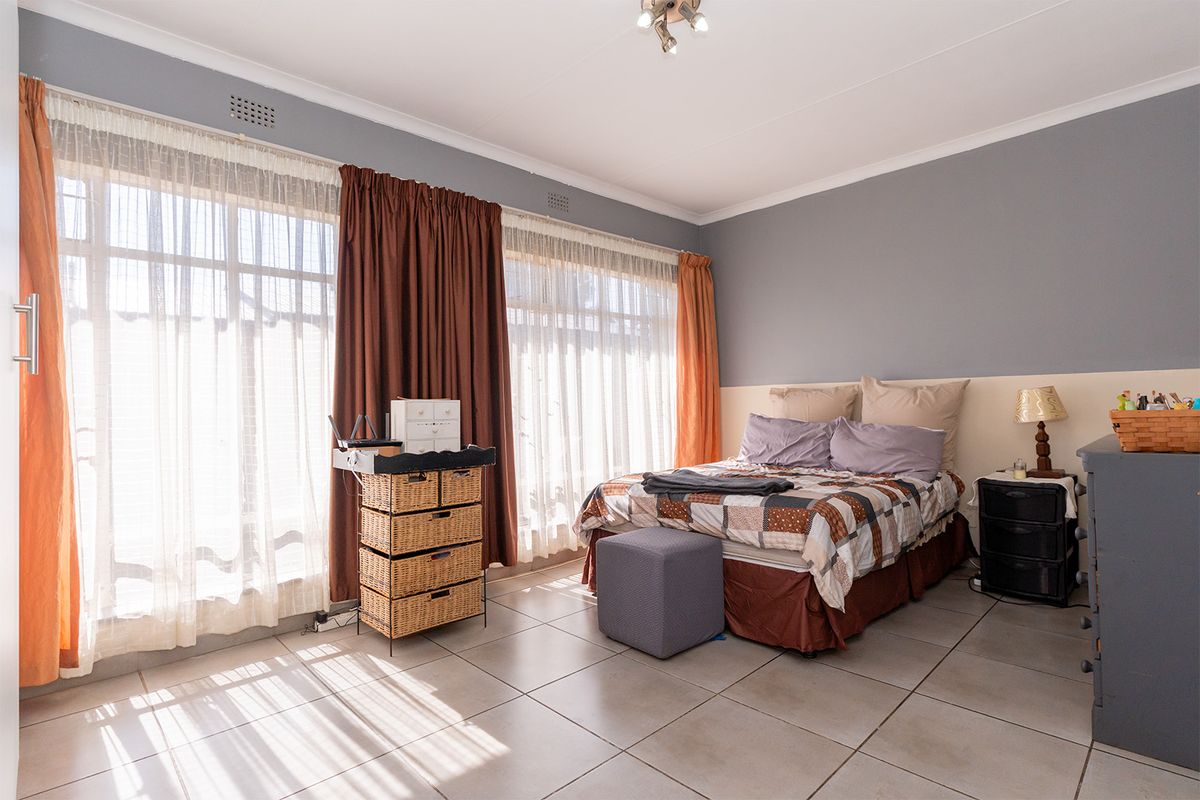 A spacious bedroom featuring large windows that provide ample natural light, tiled flooring, and neutral wall finishes.