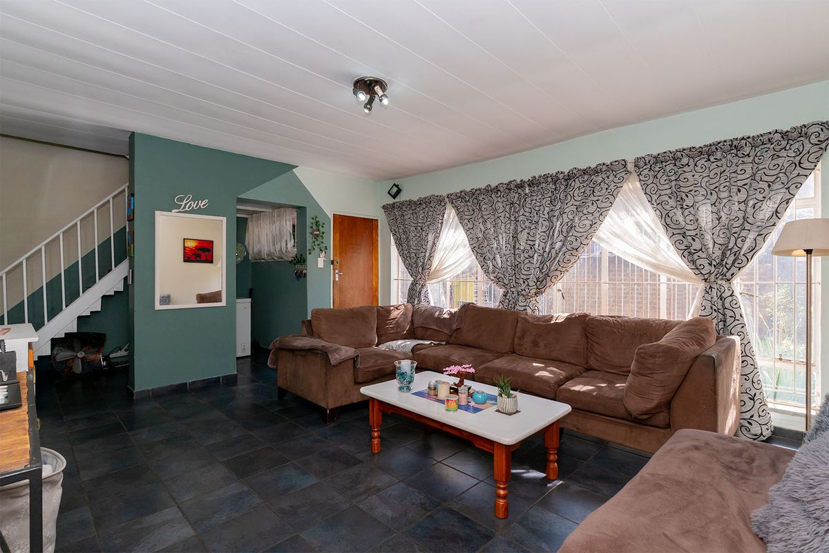 A living room featuring dark tiled flooring, a staircase, and large windows with security bars, offering a functional space with potential for modernization.