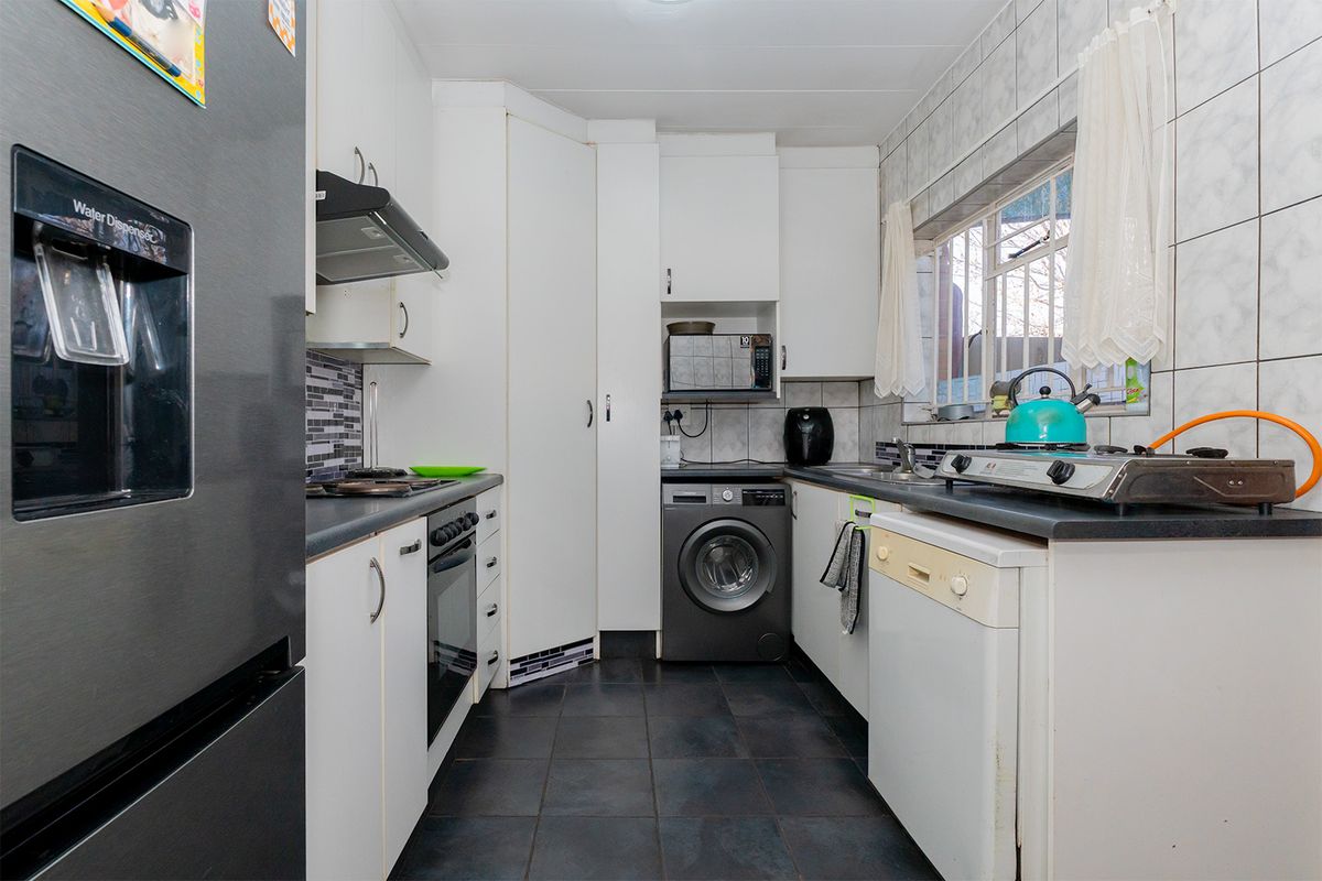 Compact kitchen featuring built-in cabinetry, dark tiled flooring, tiled backsplash, and integrated oven with extractor fan.