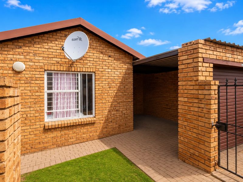 Front exterior view of a face brick townhouse featuring a paved driveway, integrated carport, secure garage access, and a small front garden area.