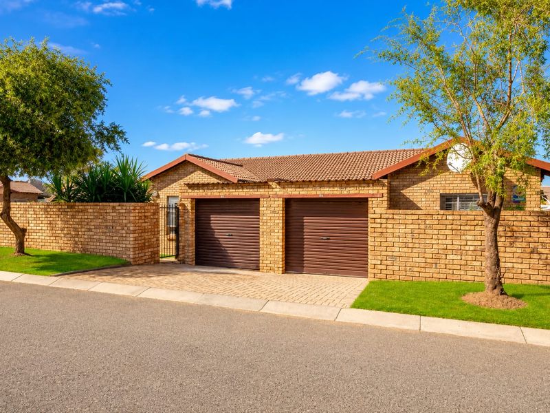 Front view of a townhouse featuring a double garage with roller doors, brick exterior, tiled roof, and a paved driveway.