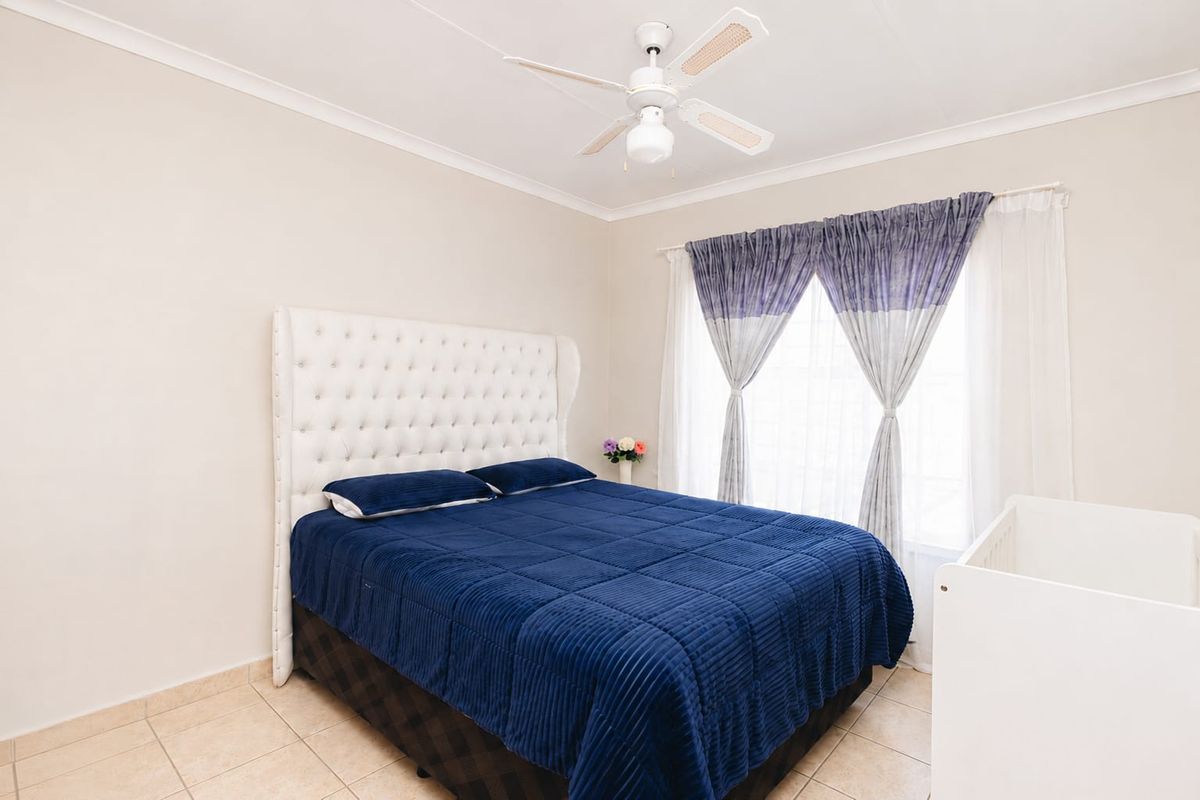 A well-lit bedroom featuring neutral wall tones, tiled flooring, and a ceiling fan, providing a comfortable and functional living space.