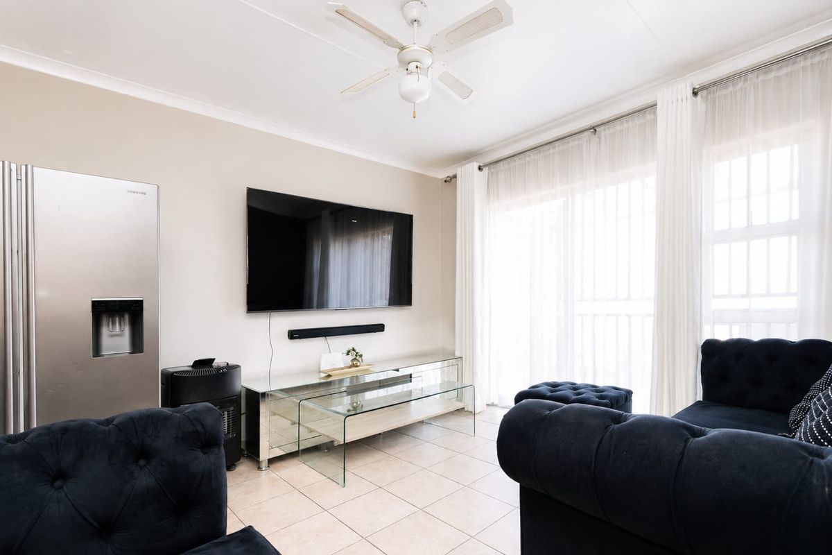 A bright living room featuring tiled flooring, a ceiling fan, and large sliding glass doors that provide ample natural light.