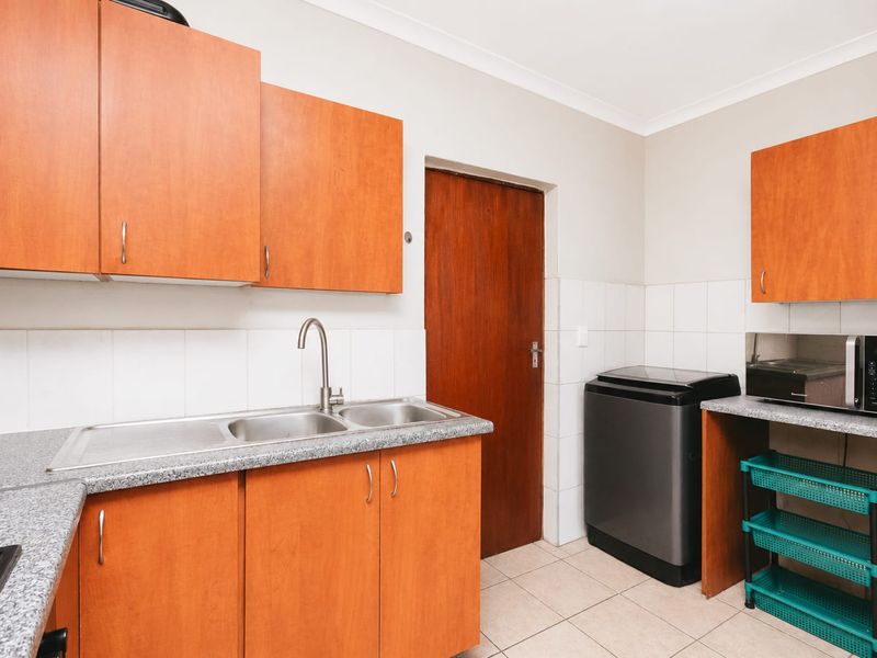 Functional scullery area featuring laminate cabinetry, durable countertops, a stainless steel double sink, and tiled splashbacks, providing practical utility space.