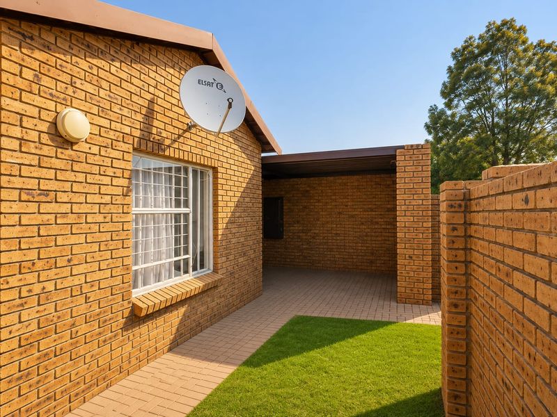 A well-maintained rear exterior view of the townhouse featuring face brick construction, a paved patio area, and a small private garden space.