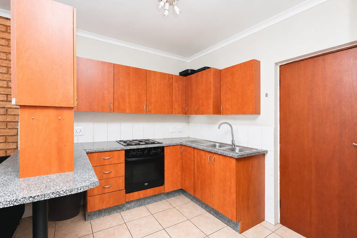 A functional kitchen featuring wood-look cabinetry, granite-style countertops, built-in oven and hob, double sink, and tiled flooring.