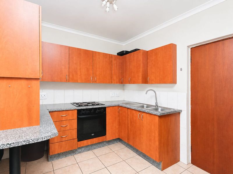 A functional kitchen featuring wood-look cabinetry, granite-style countertops, built-in oven and hob, double sink, and tiled flooring.