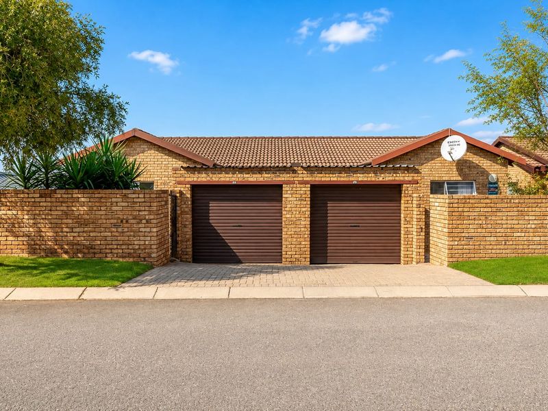 Front view of a townhouse featuring a double garage with roller doors, brick exterior, and a paved driveway.