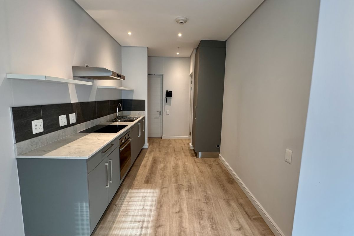 Modern galley-style kitchen featuring sleek grey cabinetry, stone countertops, integrated electric hob, oven, and extractor fan with light wood-look laminate flooring.