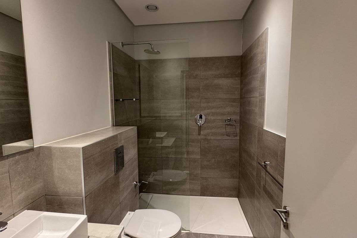 Modern bathroom featuring a walk-in shower with glass screen, wall-mounted toilet with concealed cistern, and a sleek vanity basin with contemporary tiling.