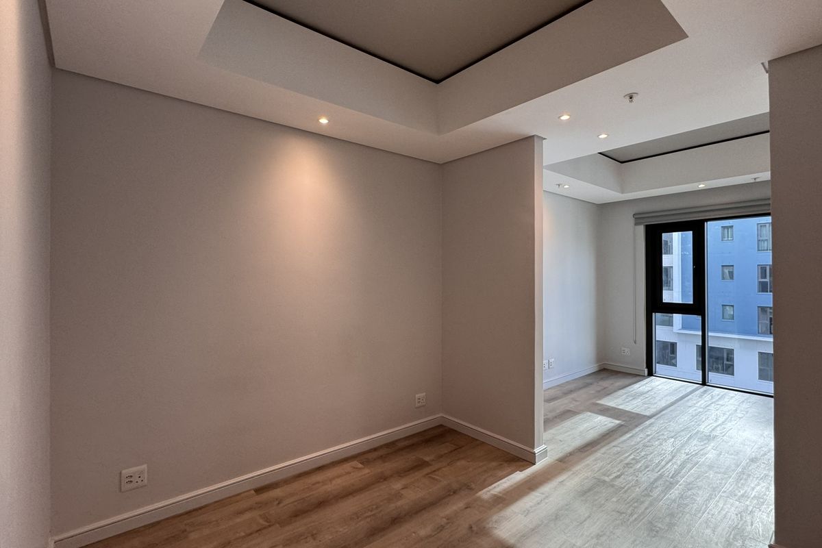 A bright, modern, and empty living area featuring recessed ceiling details, integrated lighting, and wood-look laminate flooring with access to a balcony.