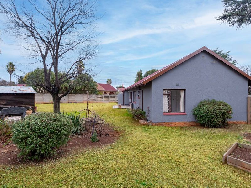 Rear view of the property featuring a spacious garden, a timber storage shed, raised garden beds, and a precast concrete boundary wall.