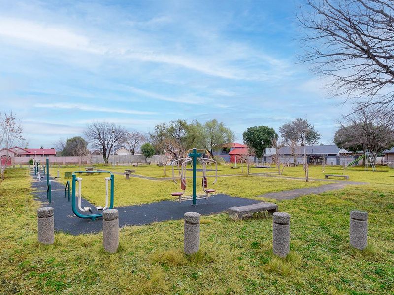 An outdoor communal sports and fitness area featuring fixed exercise equipment, paved walkways, and landscaped green space.
