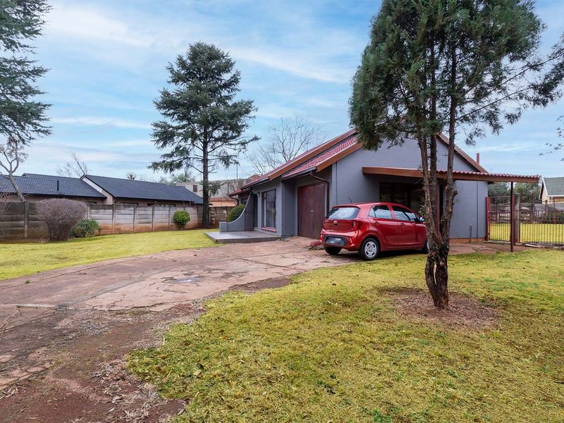 Front view of a residential property featuring a concrete driveway, attached garage, and perimeter walling set within a spacious garden area.