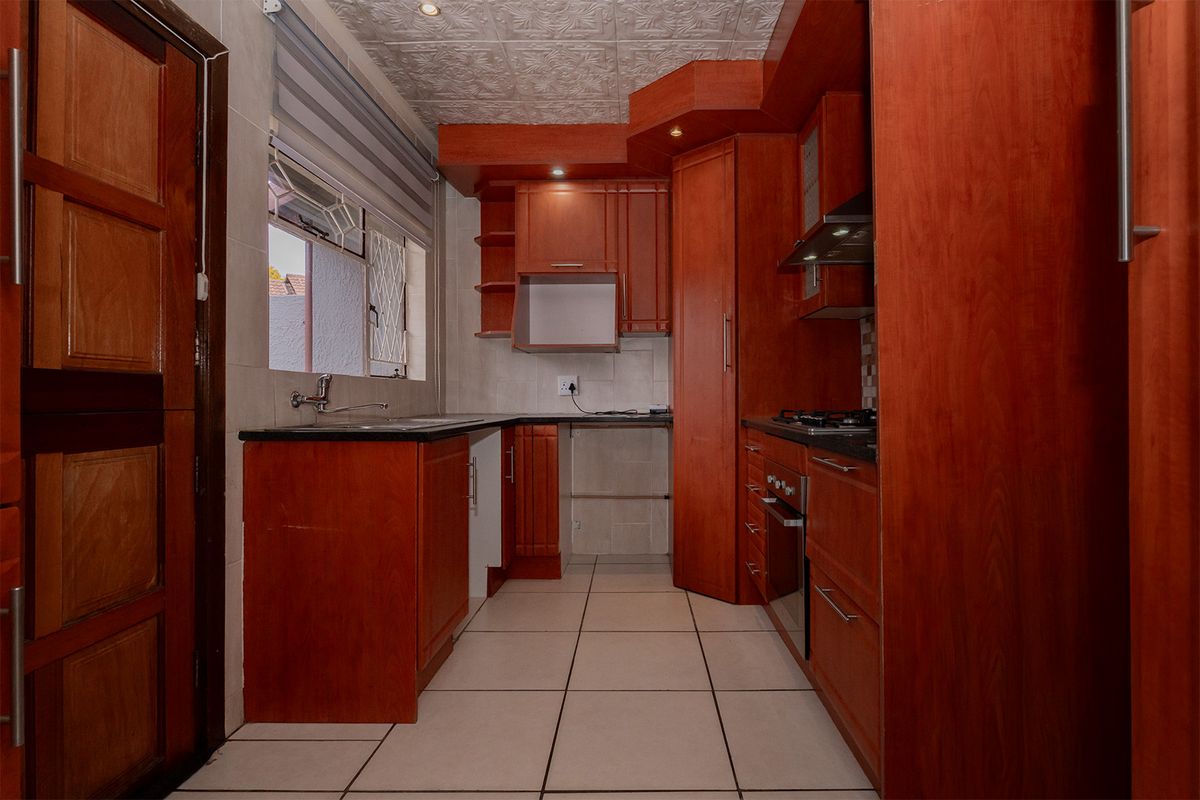 A functional kitchen featuring warm-toned wooden cabinetry, granite countertops, built-in oven, gas hob, and tiled finishes throughout.