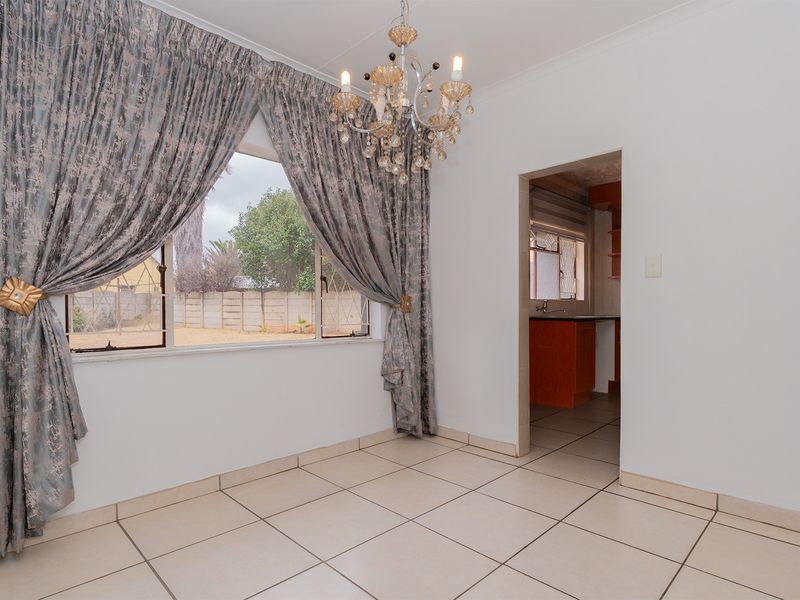 A bright dining area featuring tiled flooring, a decorative chandelier, and a view through to the adjacent kitchen space.