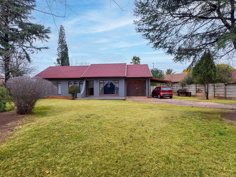 Front view of a single-story house featuring a tiled roof, concrete driveway, carport, and a large front lawn with perimeter boundary walling.