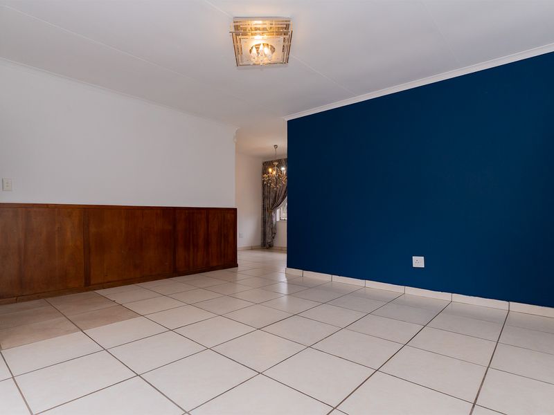 An empty living area featuring ceramic tile flooring, a blue accent wall, and traditional wooden wainscoting, leading into an adjacent room.