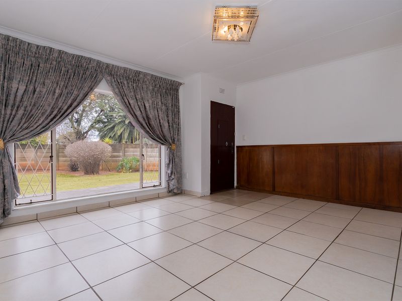 Spacious living area featuring neutral tiled flooring, classic wooden wall paneling, and direct access to the garden through a sliding glass door.